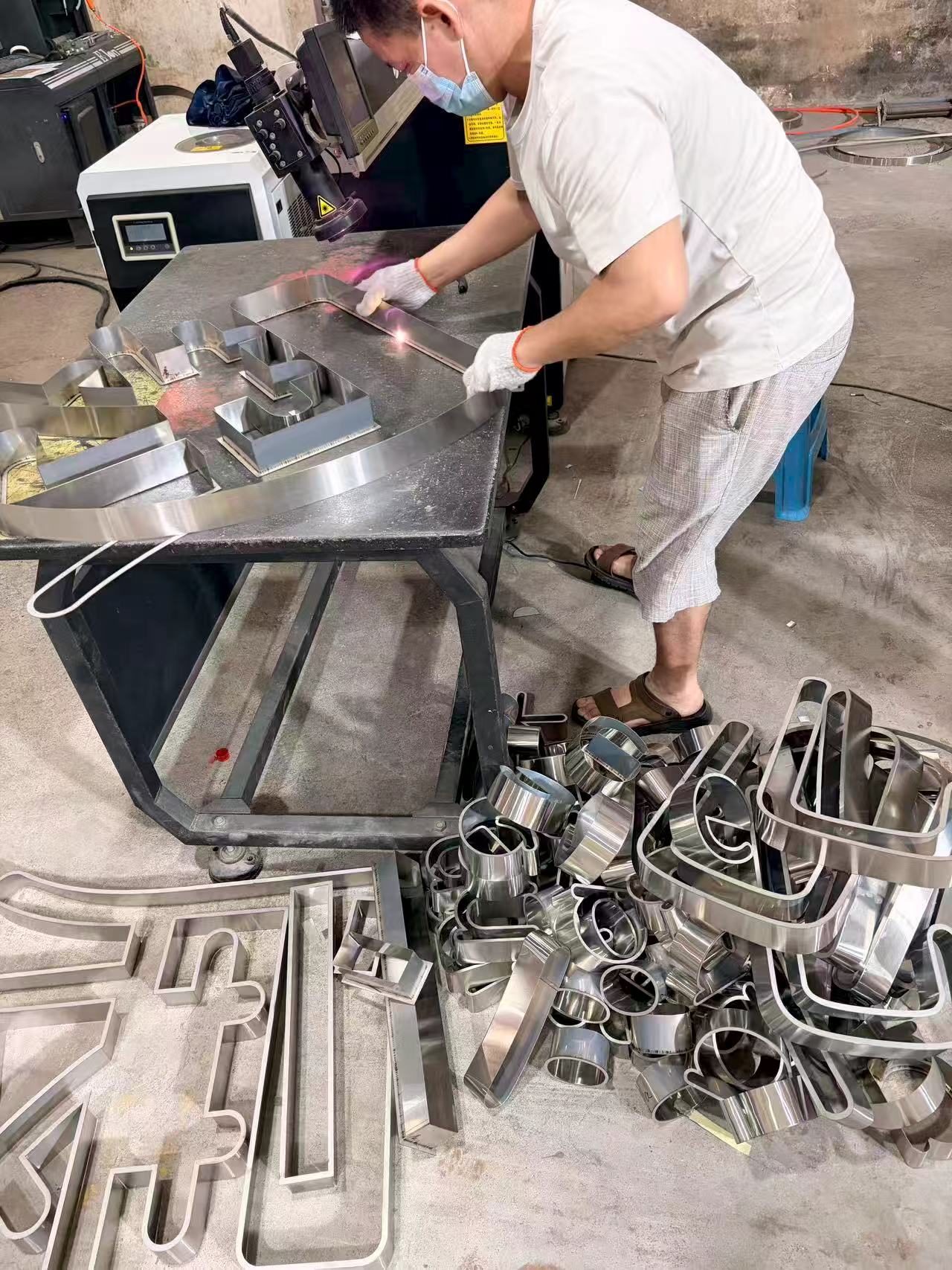 Raw stainless steel sheets and fabrication tools on workshop tables. The starting point of custom metal sign manufacturing.